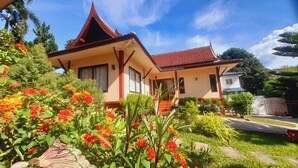 A two-story house with a red tiled roof, a porch with steps, and a garden with flowering plants. - Samui Diving Resort (Koh Samui)