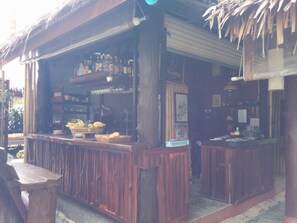 A wooden bar area with shelves of bottles, a counter with glasses, and a display of fruits. - Dolphin Bungalows (Ko Pha-ngan)