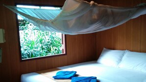 Una cama con mosquitero, una ventana con vistas a la vegetación y un ventilador de techo.