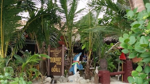 Letrero del Dolphin Bar & Grill rodeado de plantas tropicales y una estatua.