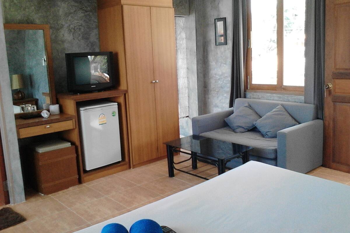 Una habitación de hotel compacta con cama, un escritorio pequeño con televisor, refrigerador, sofá y ventana con cortinas.