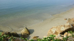Una playa con agua cristalina, rocas y barcos.
