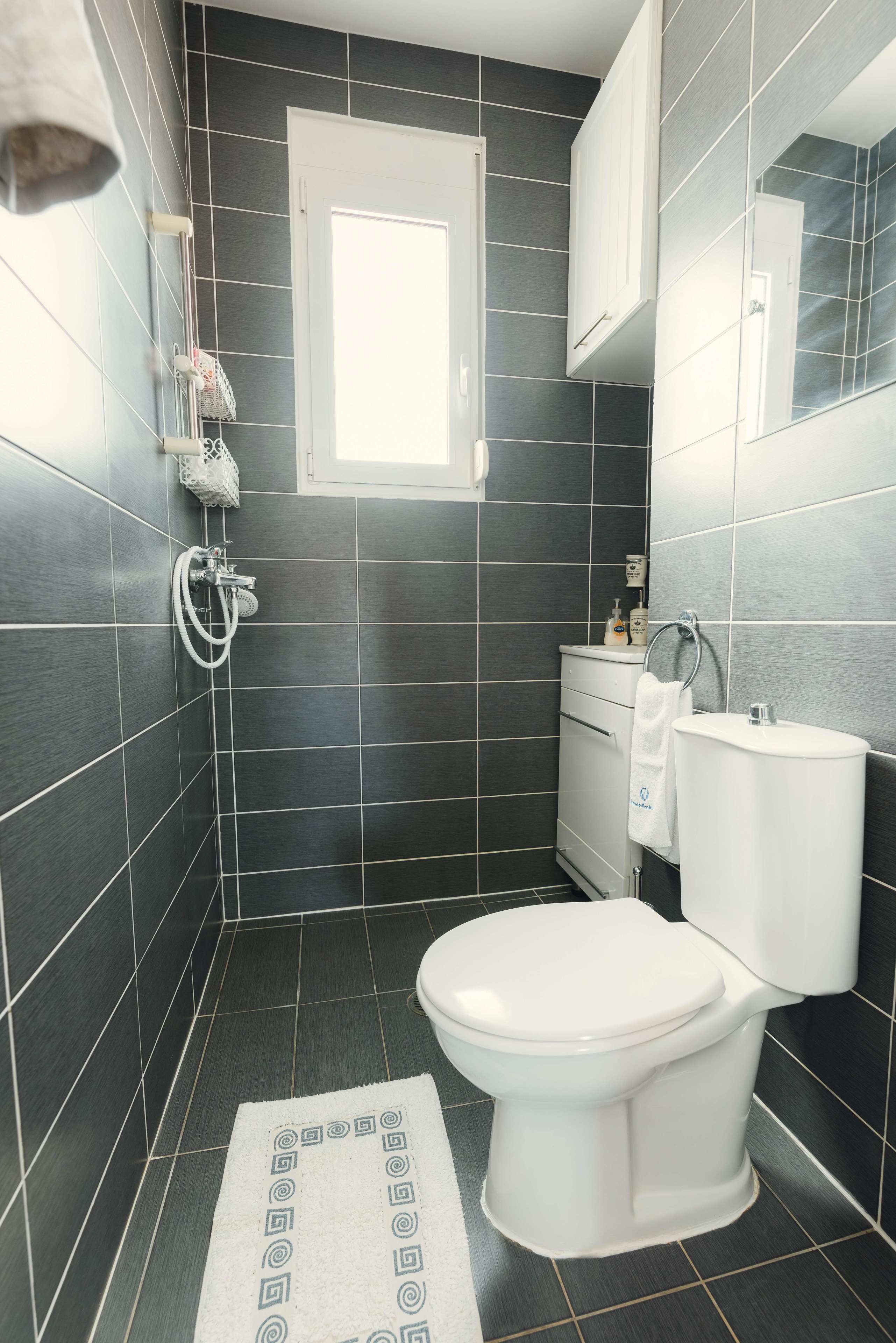 Un bany modern amb rajoles fosques, un vàter blanc, un lavabo i una dutxa.