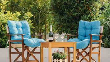 Un área de estar al aire libre con dos sillones azules acolchados y una mesa de madera, con abundante follaje y una piscina de fondo.