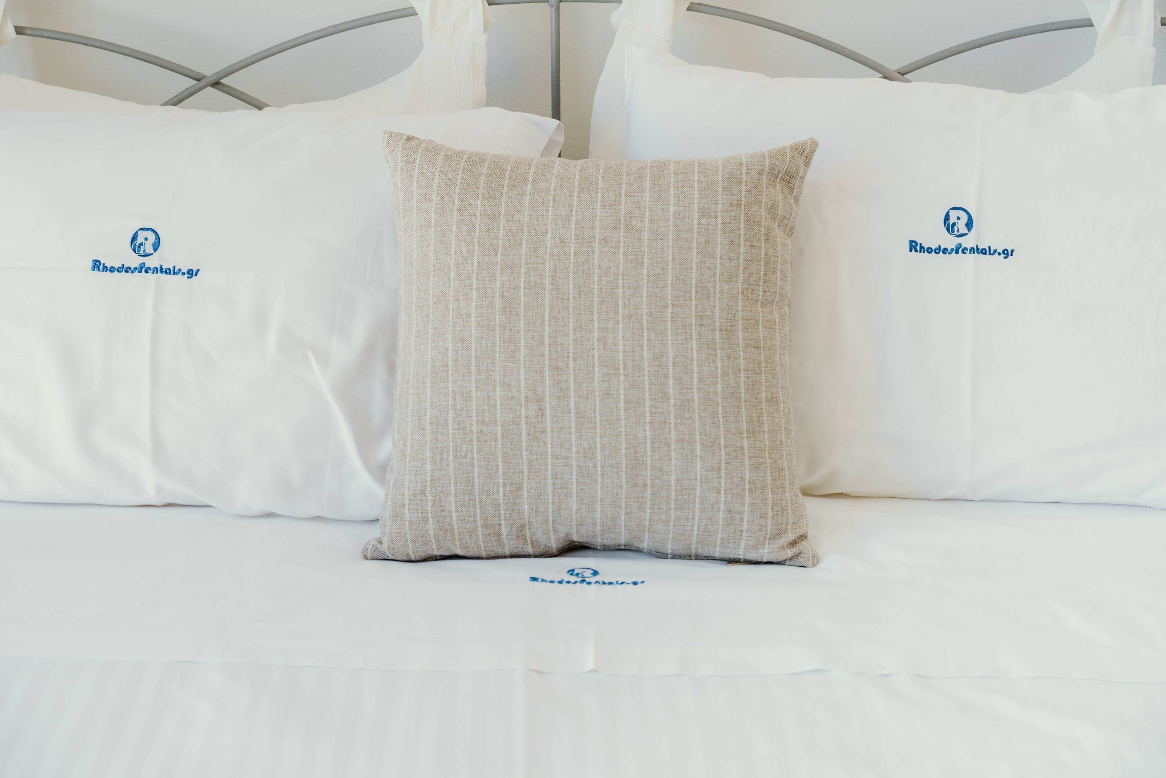 Una cama con ropa blanca y dos almohadas, una con textura y la otra lisa.