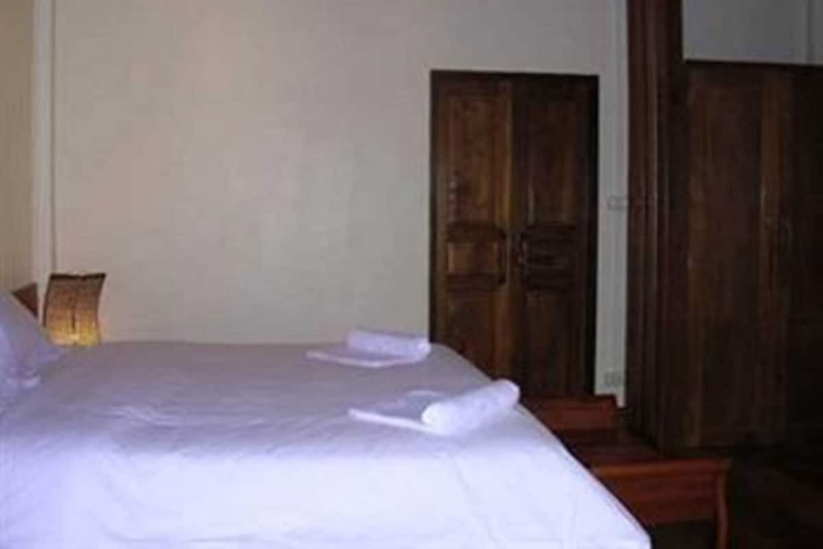 Una habitación con cama, puerta de madera y mesita de noche.