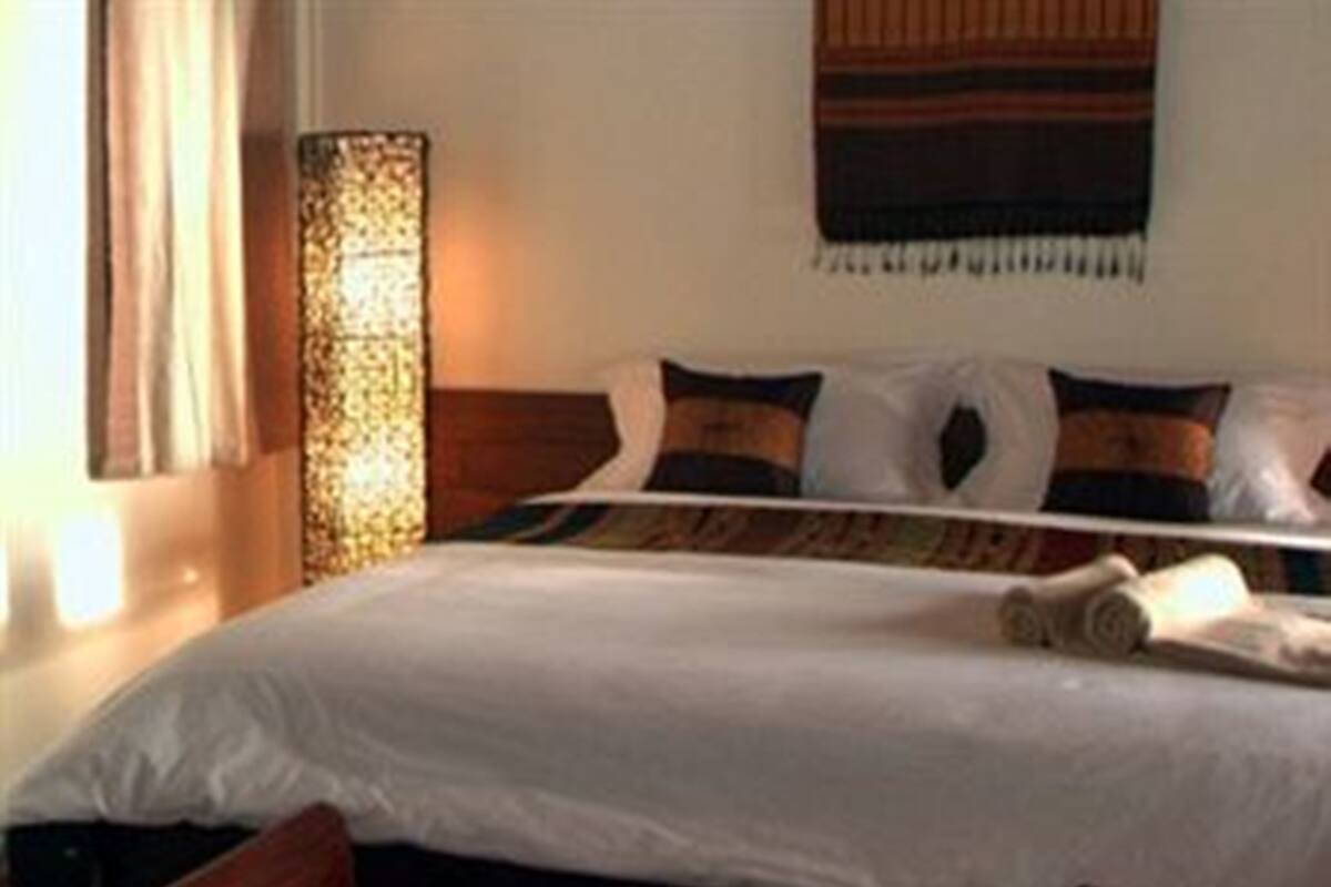 Una cama bien hecha con edredón blanco, cabecera de madera y manta decorativa.