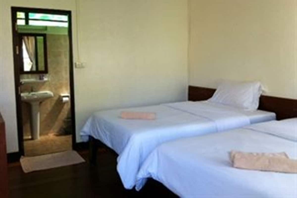 Una habitación de hotel con dos camas individuales, un baño pequeño con lavabo, y una puerta que da a otra habitación.