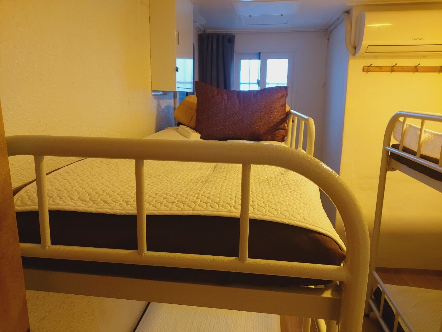 Un letto a castello con materasso e cuscini, una finestra con tende e un condizionatore d'aria a parete.
