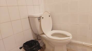 A bathroom with a toilet, a trash bin, and tiled walls.
