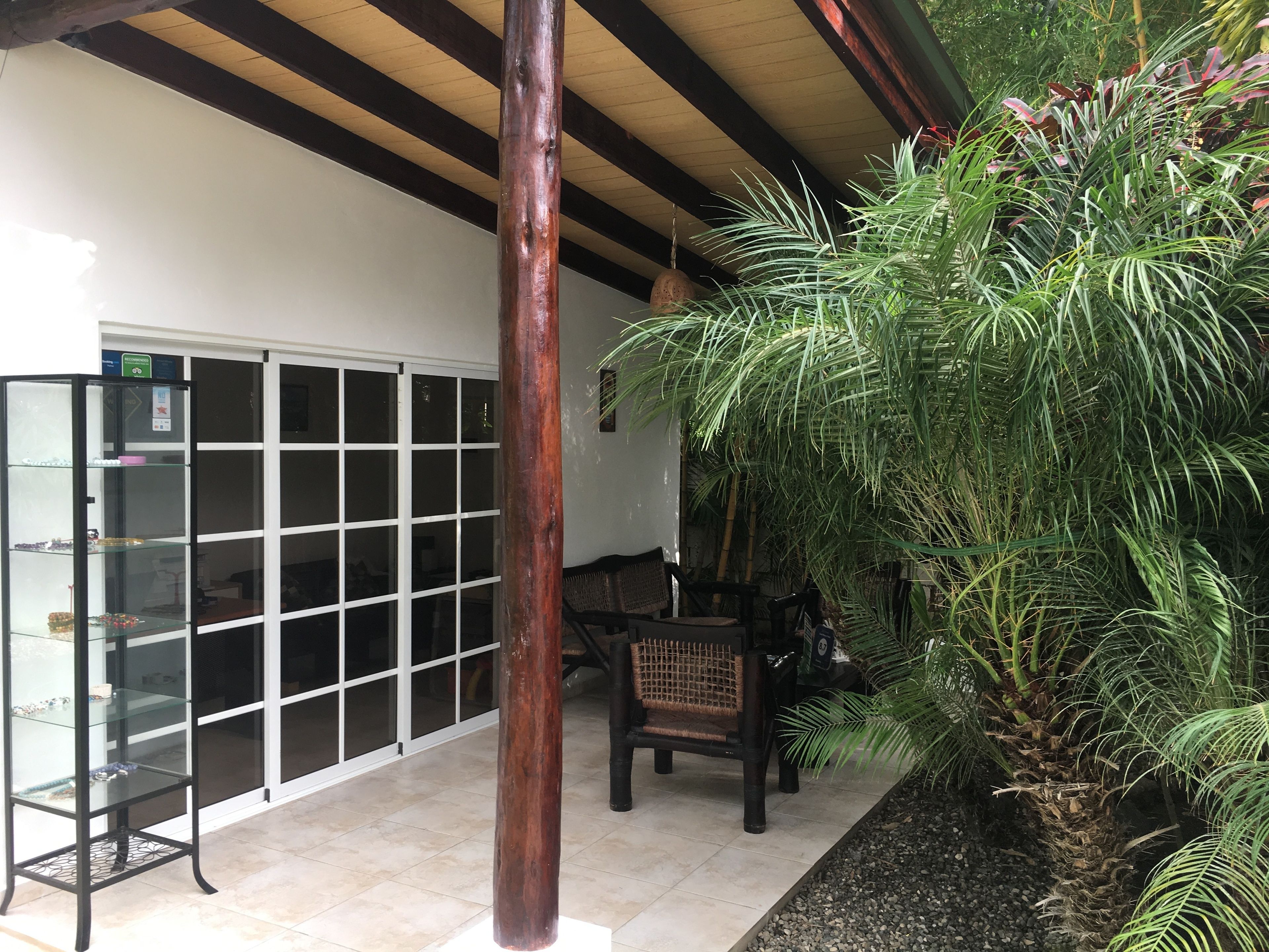 A covered patio area with a glass display case, a wooden bench, and a large plant.