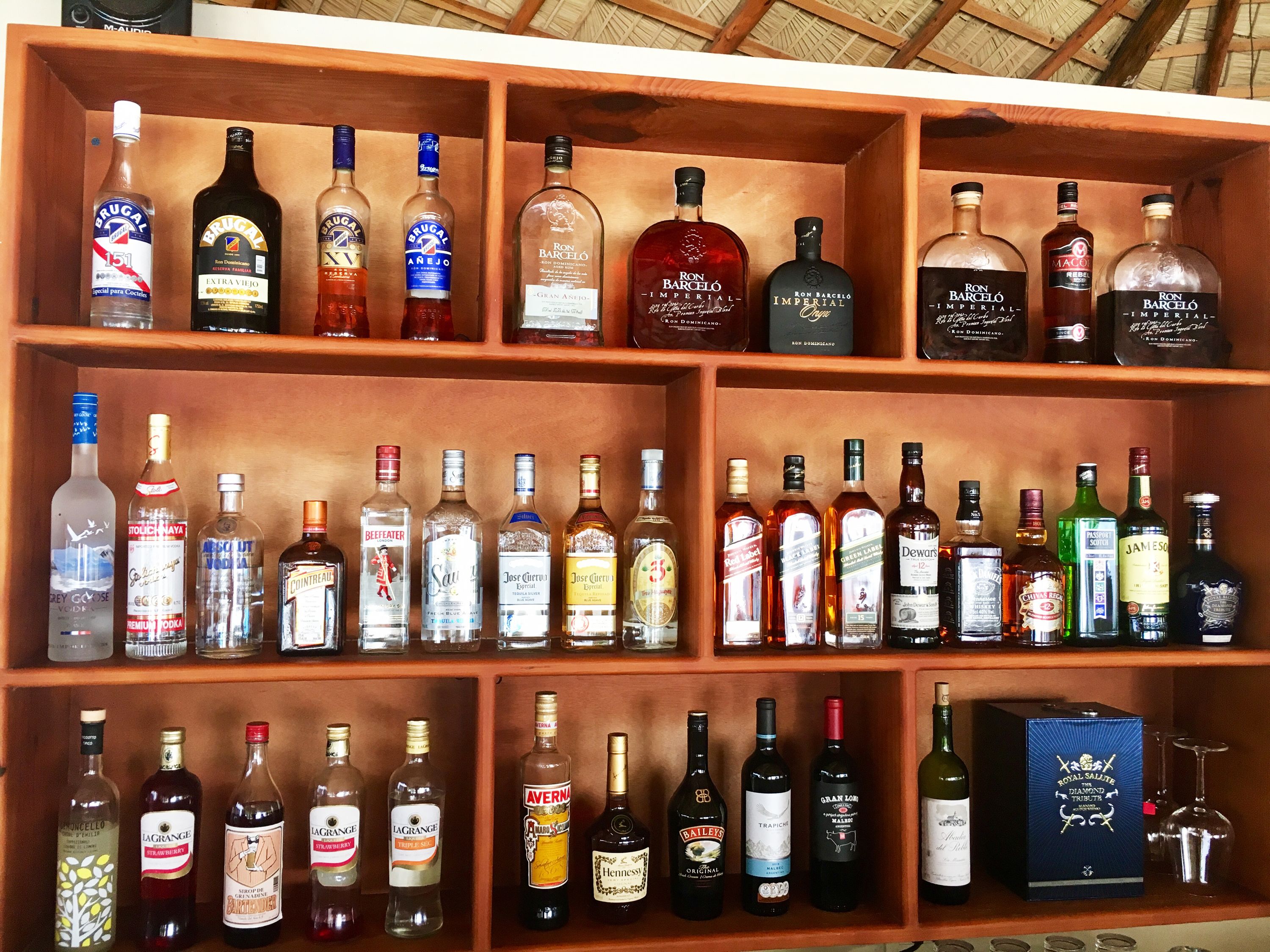 A wooden liquor cabinet with multiple shelves containing various bottles of alcohol.