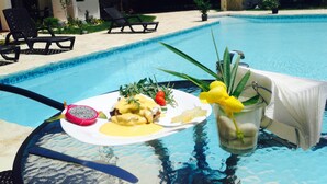 Taula de dinar amb un plat de menjar, una beguda i un parasol de palla en un ambient de piscina.