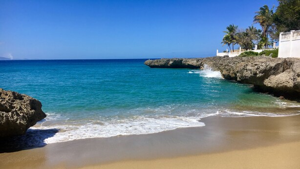 Una platja amb aigua turquesa cristal·lina, sorra daurada i roques a la vora.