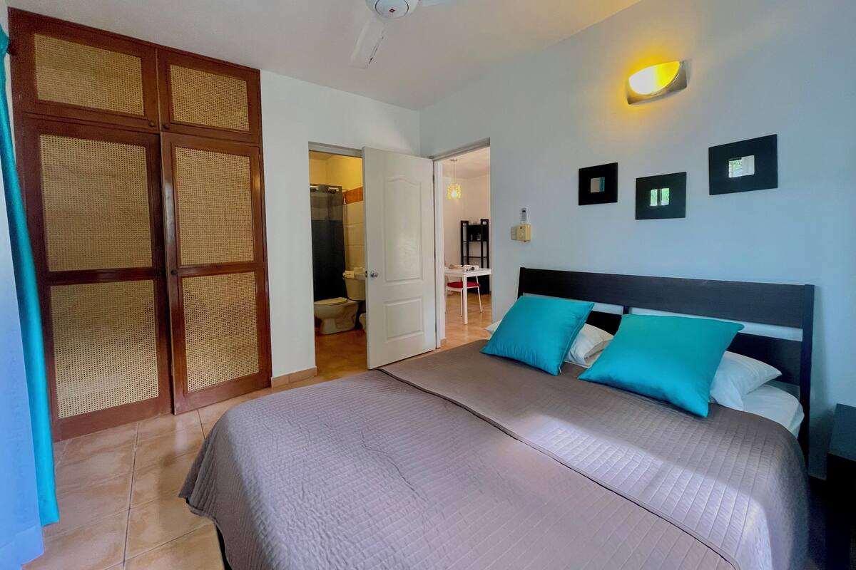 Un dormitorio con cama, ventilador de techo, lámpara de pared y puerta que da a un baño.