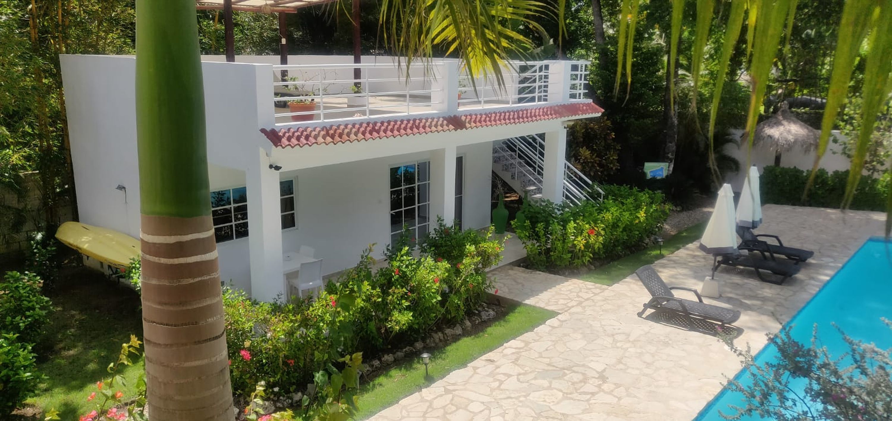 Un bâtiment blanc à deux étages, avec un toit recouvert de tuiles rouges, un balcon et un escalier.