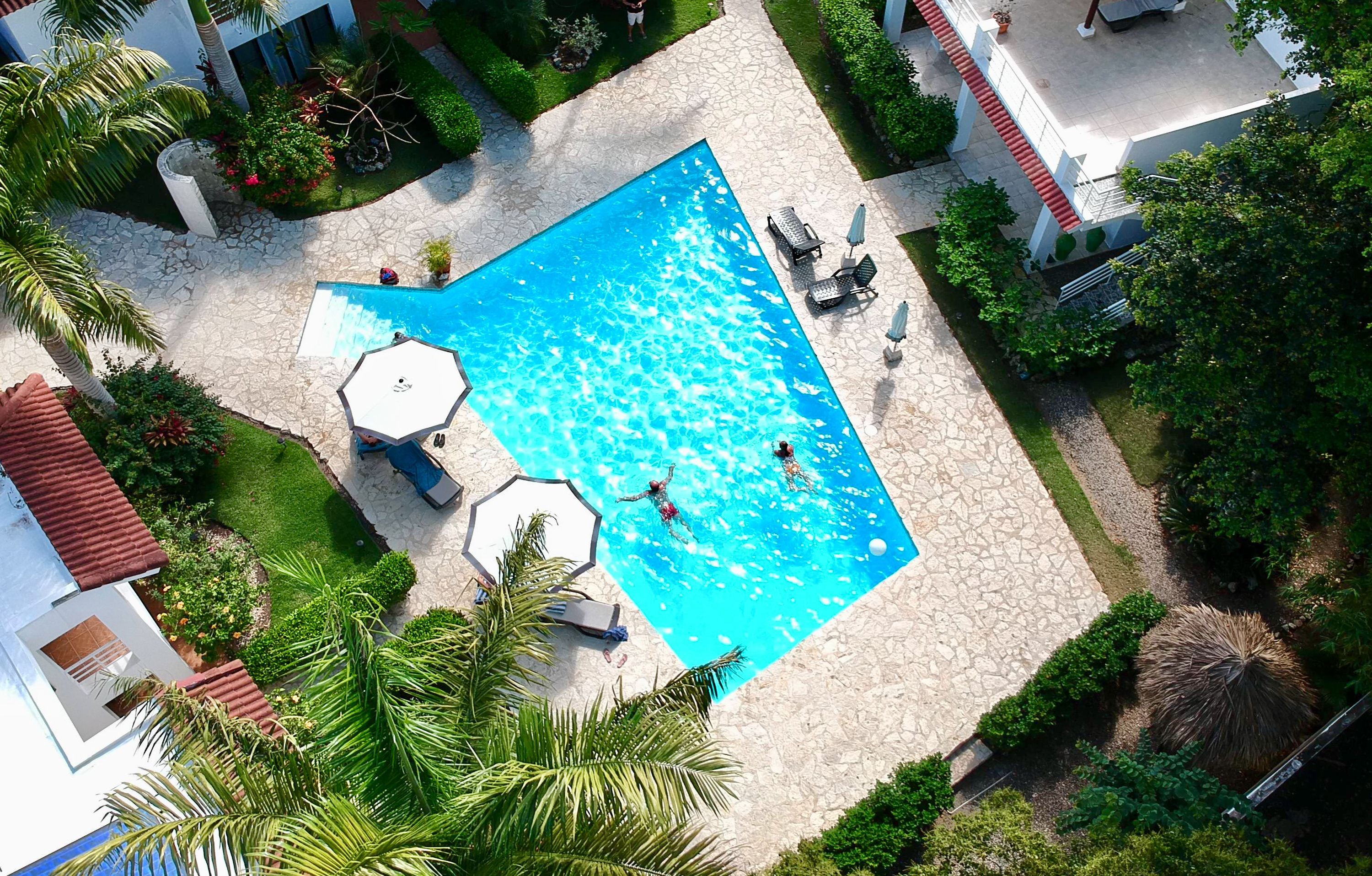 An aerial view of a swimming pool surrounded by a stone patio, with lounge chairs and umbrellas.