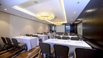 A conference room with multiple tables, chairs, and a large screen.