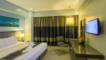 A hotel room with a bed, a desk, a chair, a TV, and a painting on the wall.