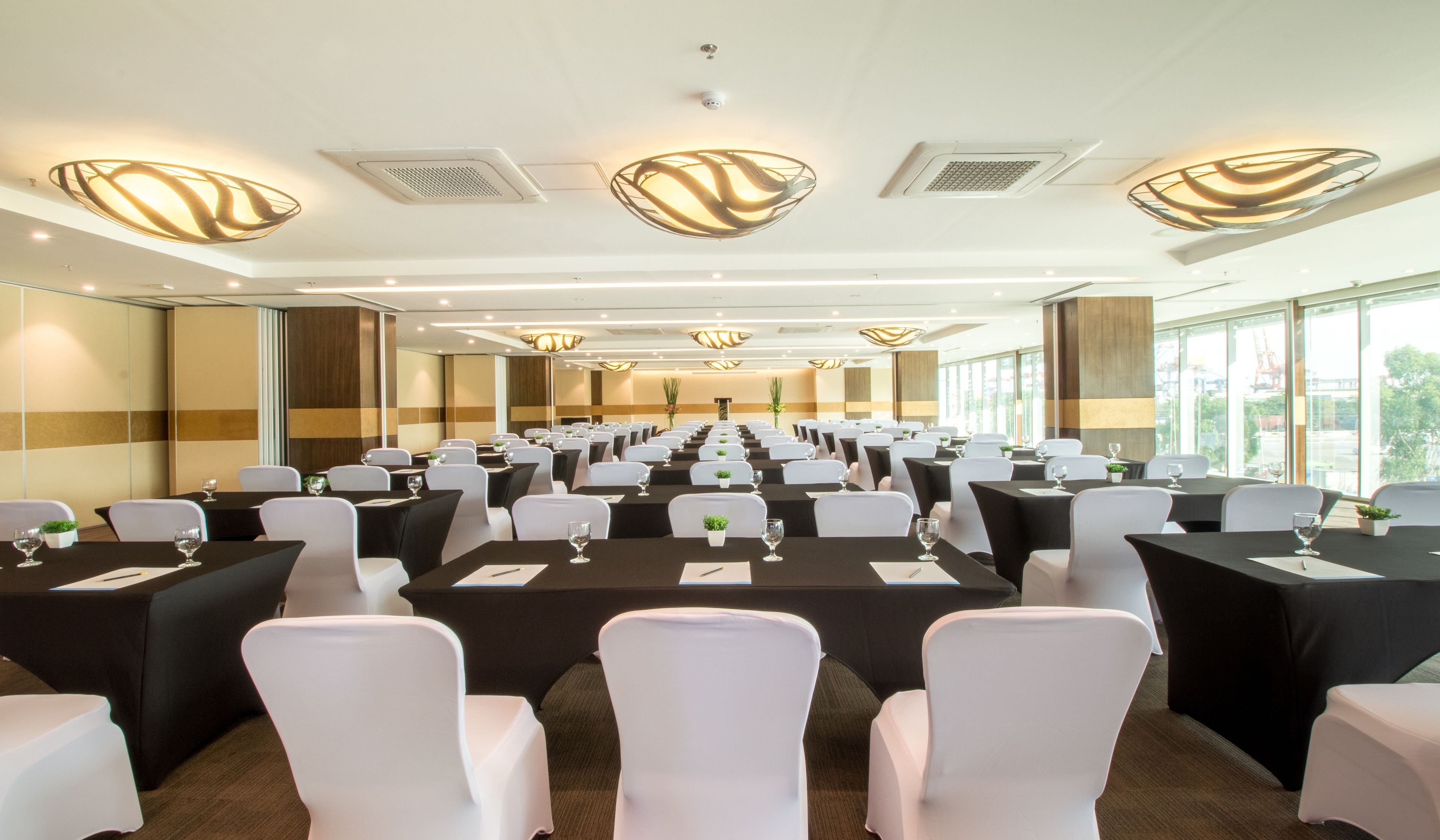 A conference room with rows of tables and chairs, large windows, and modern lighting fixtures.