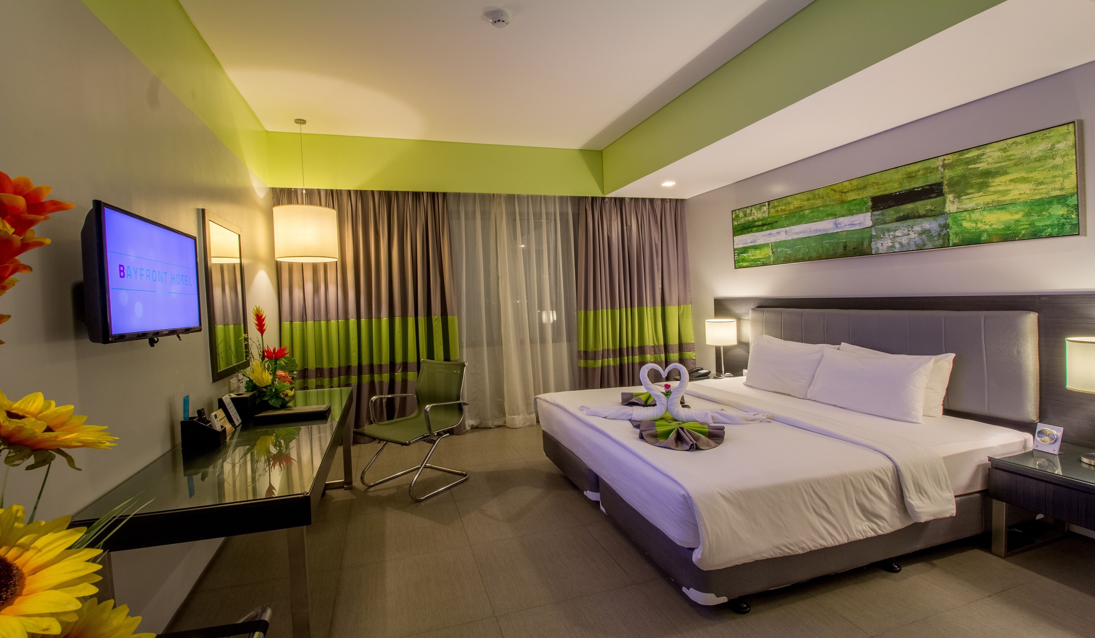 Een hotelkamer met een bed, een bureau, een stoel, een televisie en een schilderij aan de muur.
