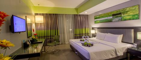 Een hotelkamer met een bed, een bureau, een stoel, een televisie en een schilderij aan de muur.
