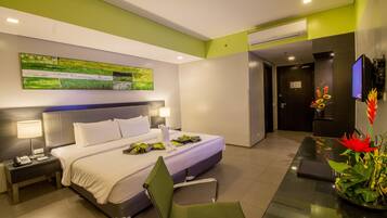 Una habitación de hotel moderna con una cama grande, mesitas de noche con lámparas, un televisor de pantalla plana, un escritorio con una silla y una pared verde con un cuadro.