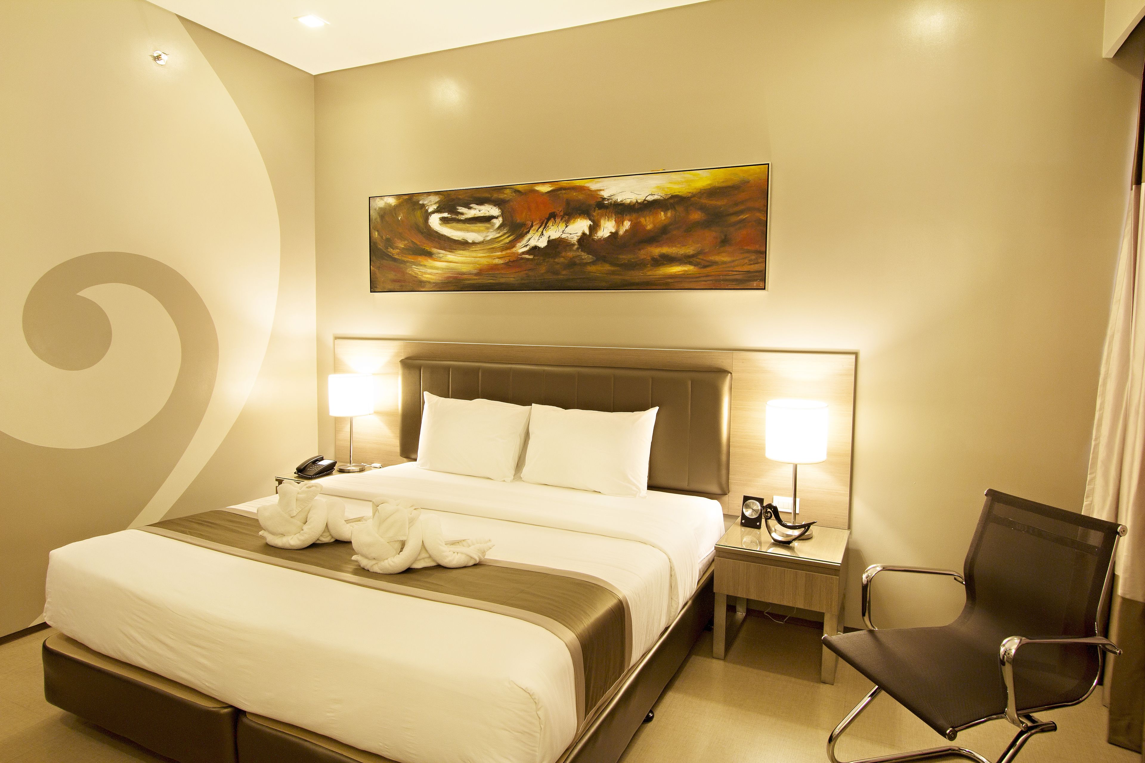 A hotel room with a large bed, two bedside lamps, a chair, and a painting on the wall.