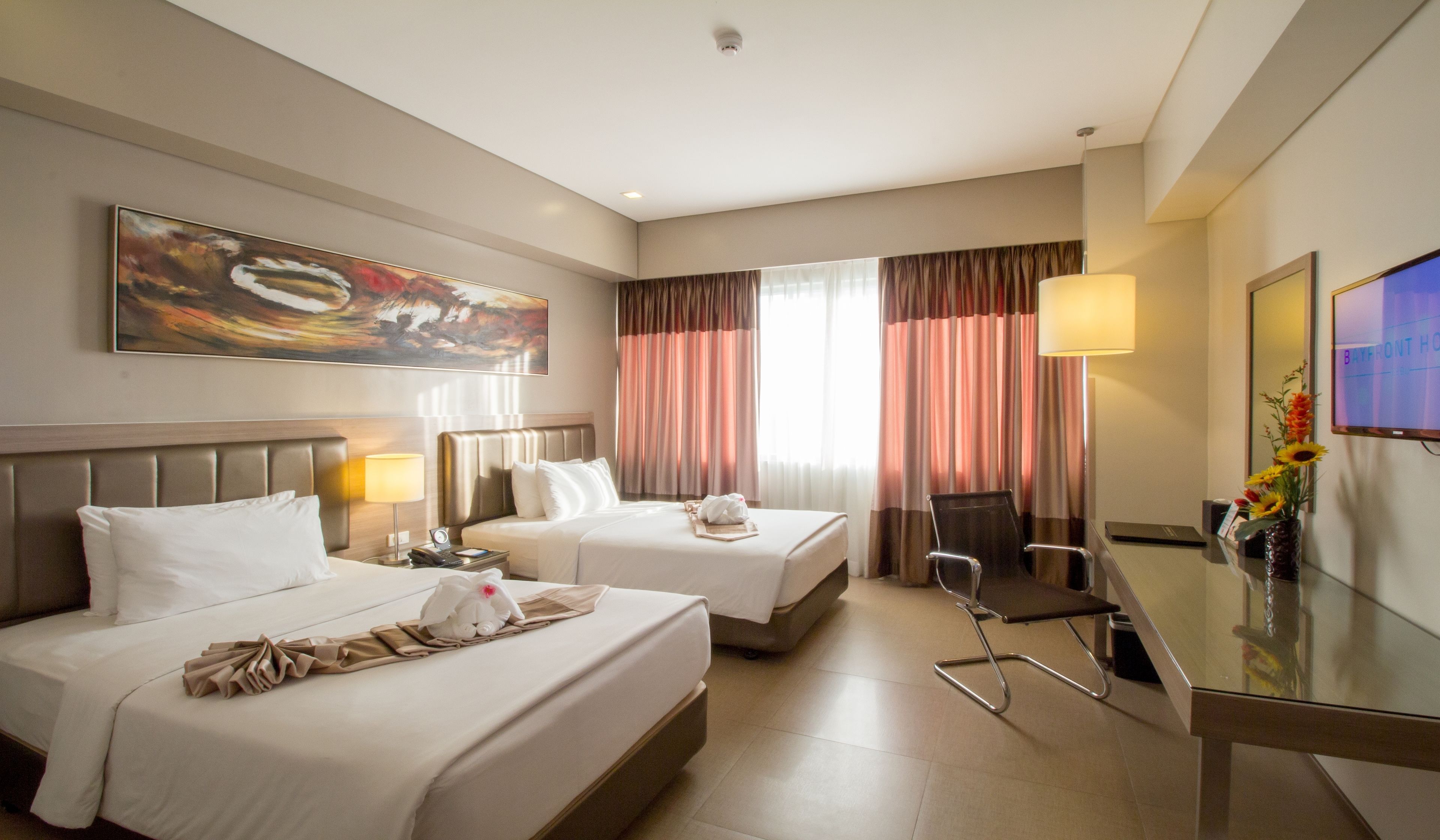 A hotel room with two beds, a desk, a chair, a TV, and a painting on the wall.