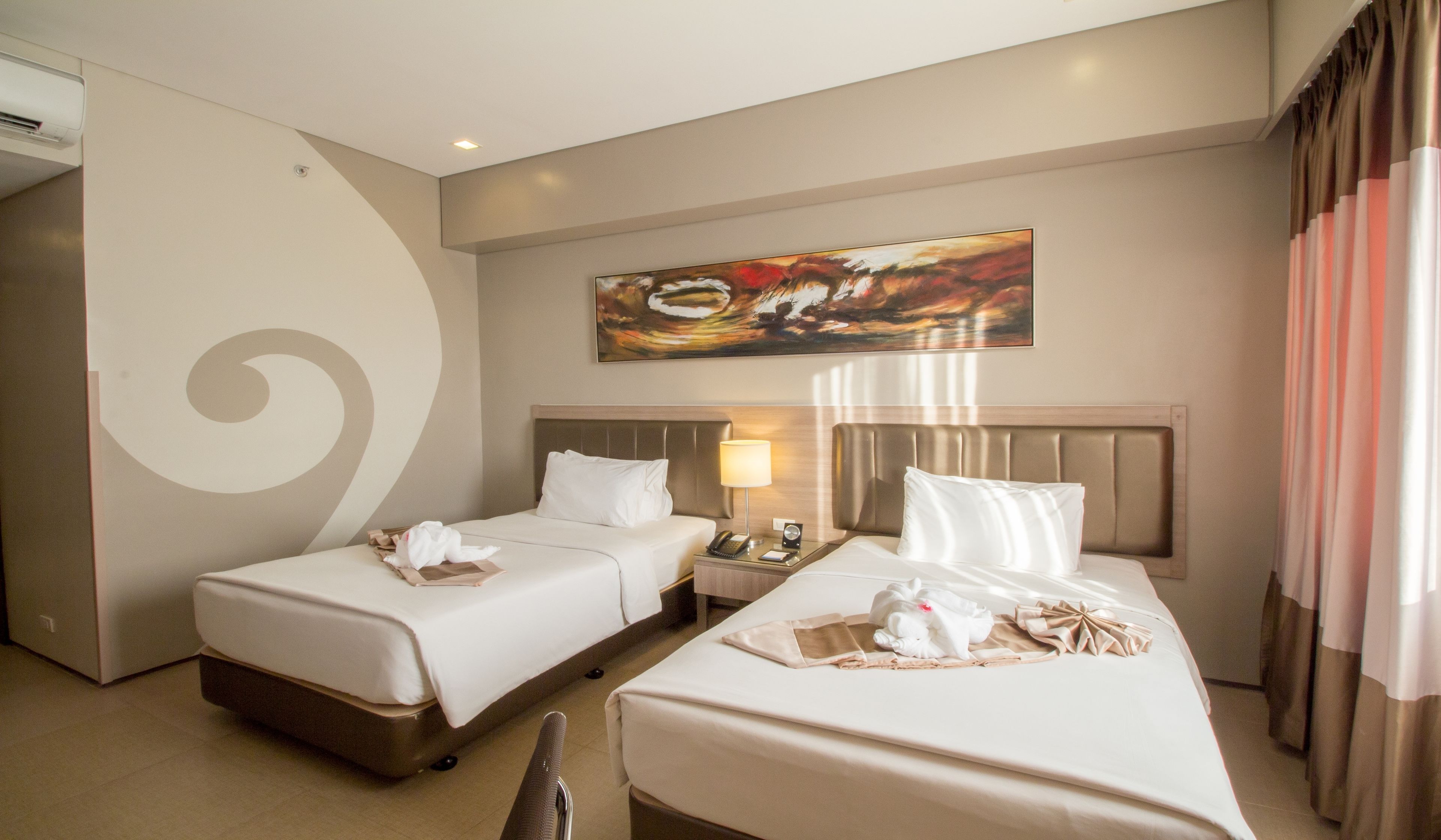 A hotel room with two beds, a painting on the wall, a nightstand, and a curtain.