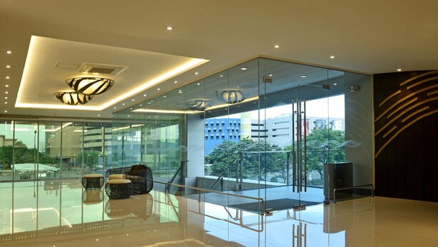 A modern lobby with glass walls, a seating area with woven chairs, and a view of the cityscape.