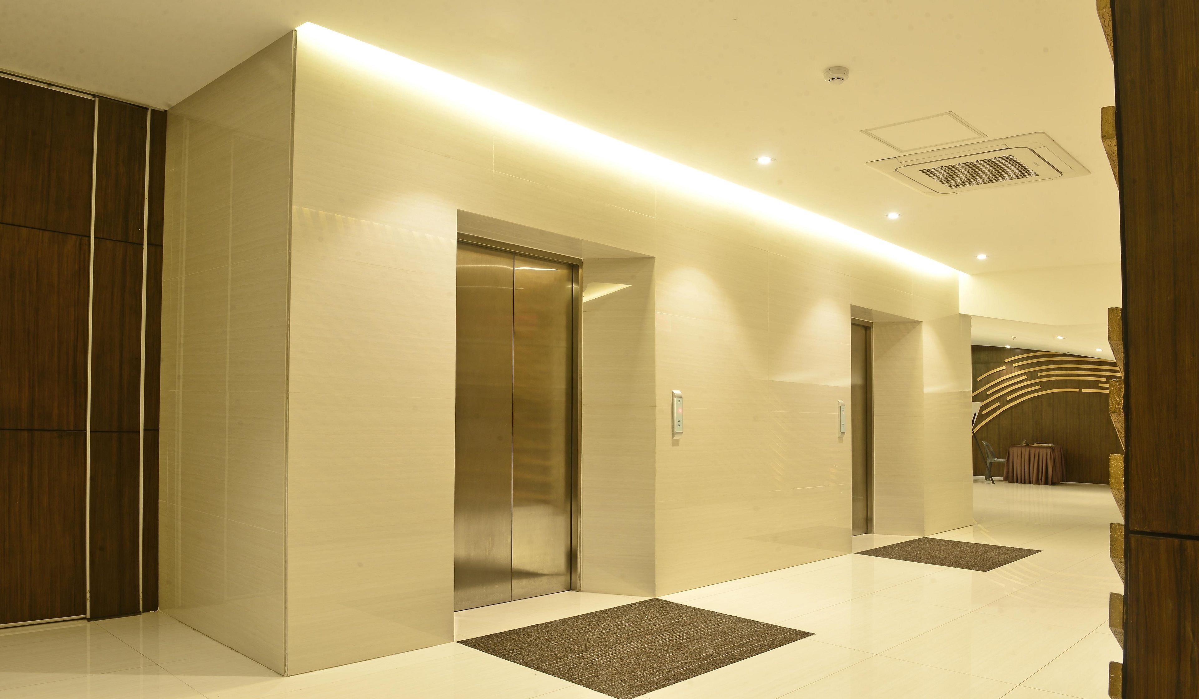 Een moderne lift in een hal met een lichtgekleurde vloer en een donkere mat ervoor.