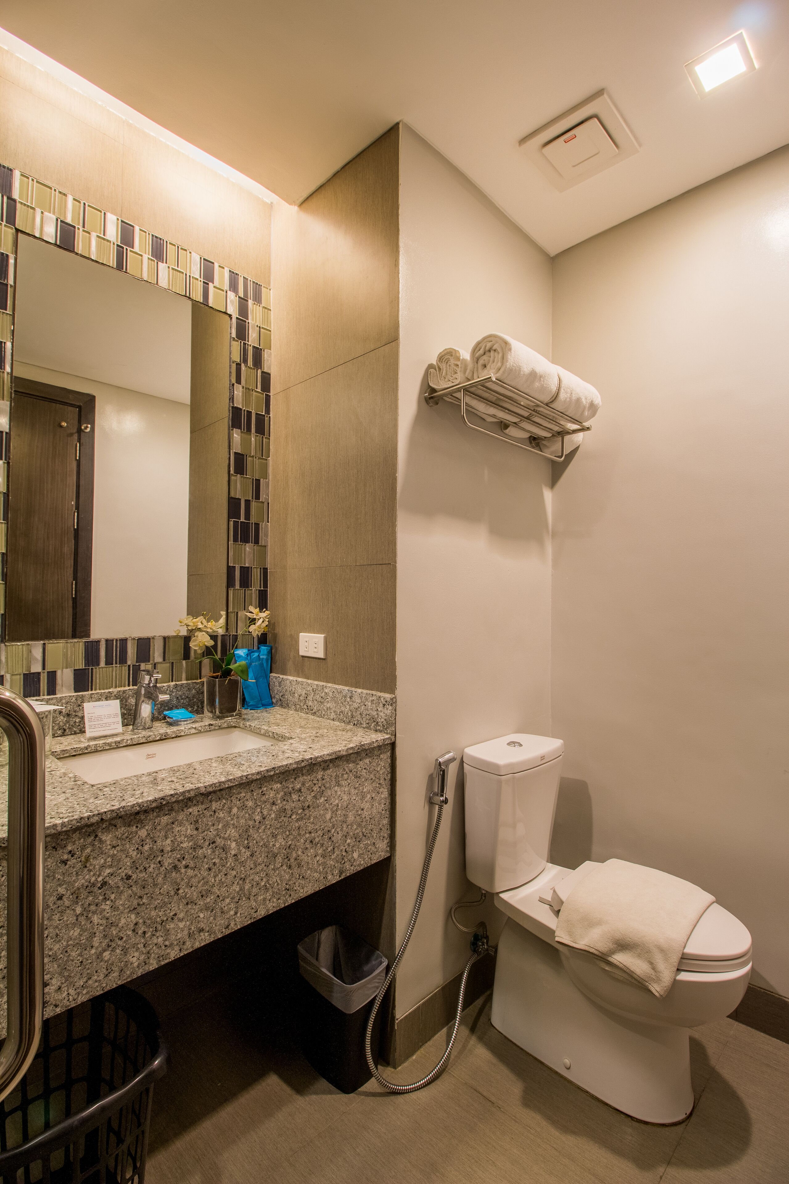 A bathroom with a granite countertop, a sink, a mirror, a toilet, and a towel rack.