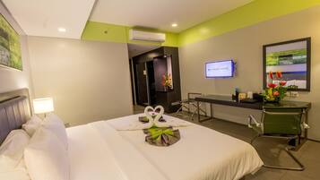 A hotel room with a bed, a desk, a chair, a TV, and a wall-mounted air conditioner.