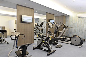 A gym with various exercise machines, including treadmills and stationary bikes, arranged in a spacious room with mirrors on the walls.