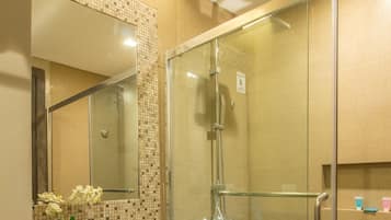 Une salle de bain moderne avec une douche à parois de verre, un comptoir en granit et une petite poubelle.
