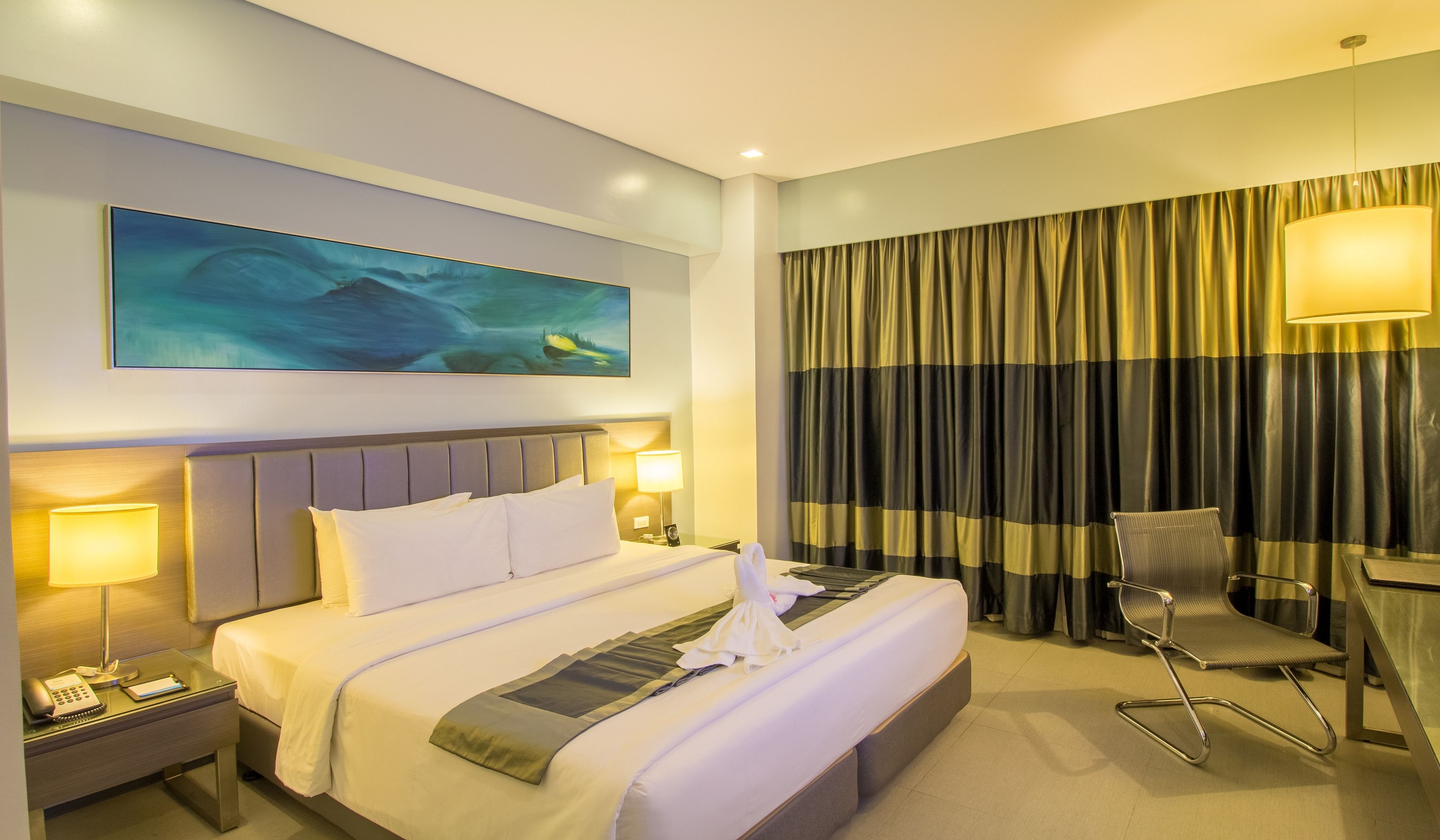Une chambre d’hôtel avec un lit, des lampes de chevet, un bureau avec une chaise, un tableau au mur et des rideaux.