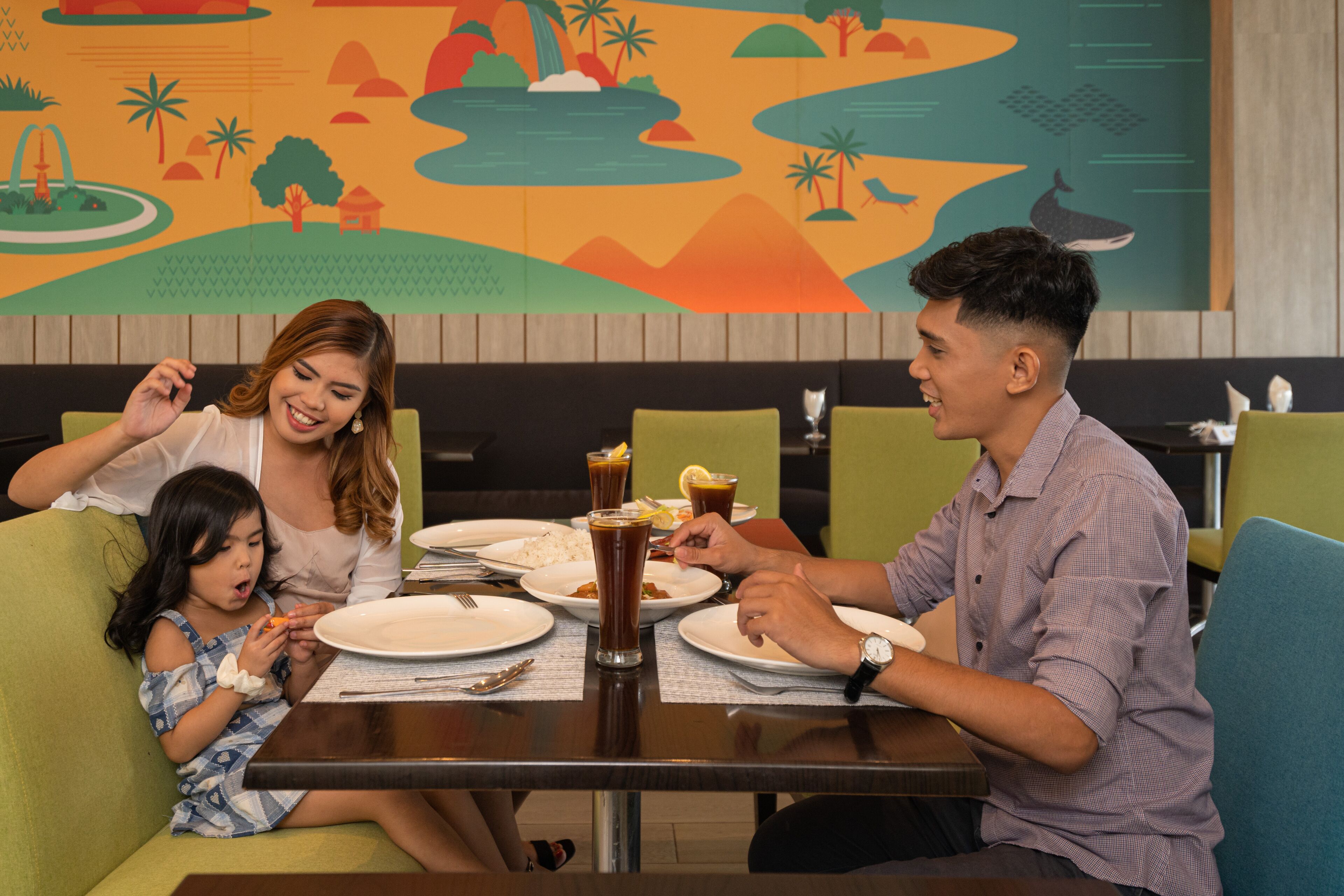 A family dining at a restaurant with a mural on the wall.