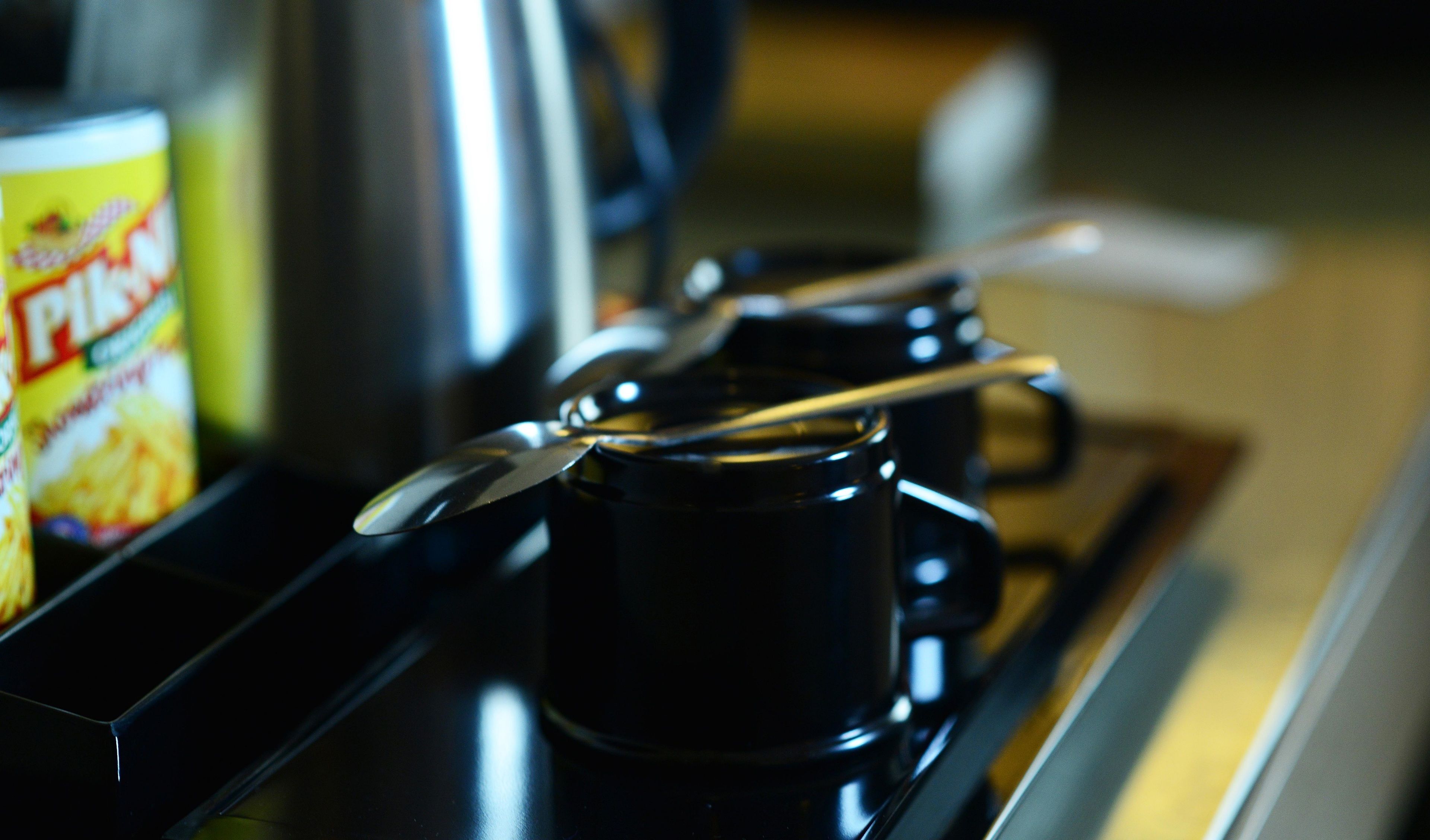 Una encimera de cocina con una lata de PIKNIK, una cafetera negra y una cuchara sobre una taza.