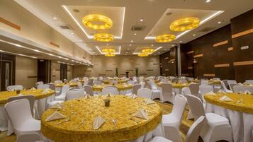 Une salle de banquet avec des tables rondes recouvertes de nappes dorées, des chaises blanches et des luminaires modernes.