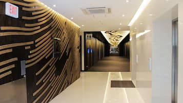 A modern hotel corridor with an exit sign, a wooden wall design, and a shiny floor.
