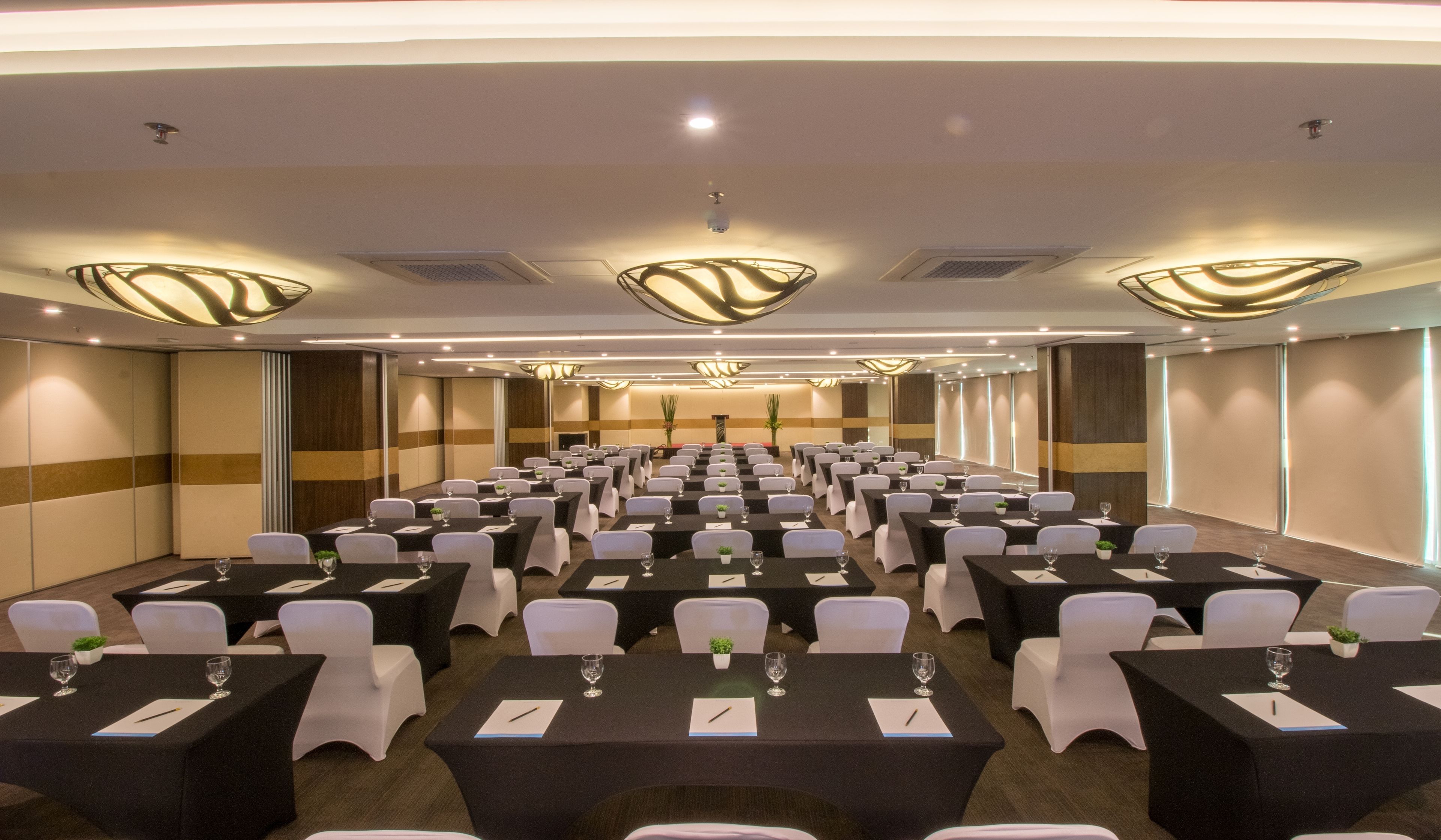 Une salle de conférence avec des rangées de tables, des chaises blanches et des nappes noires.