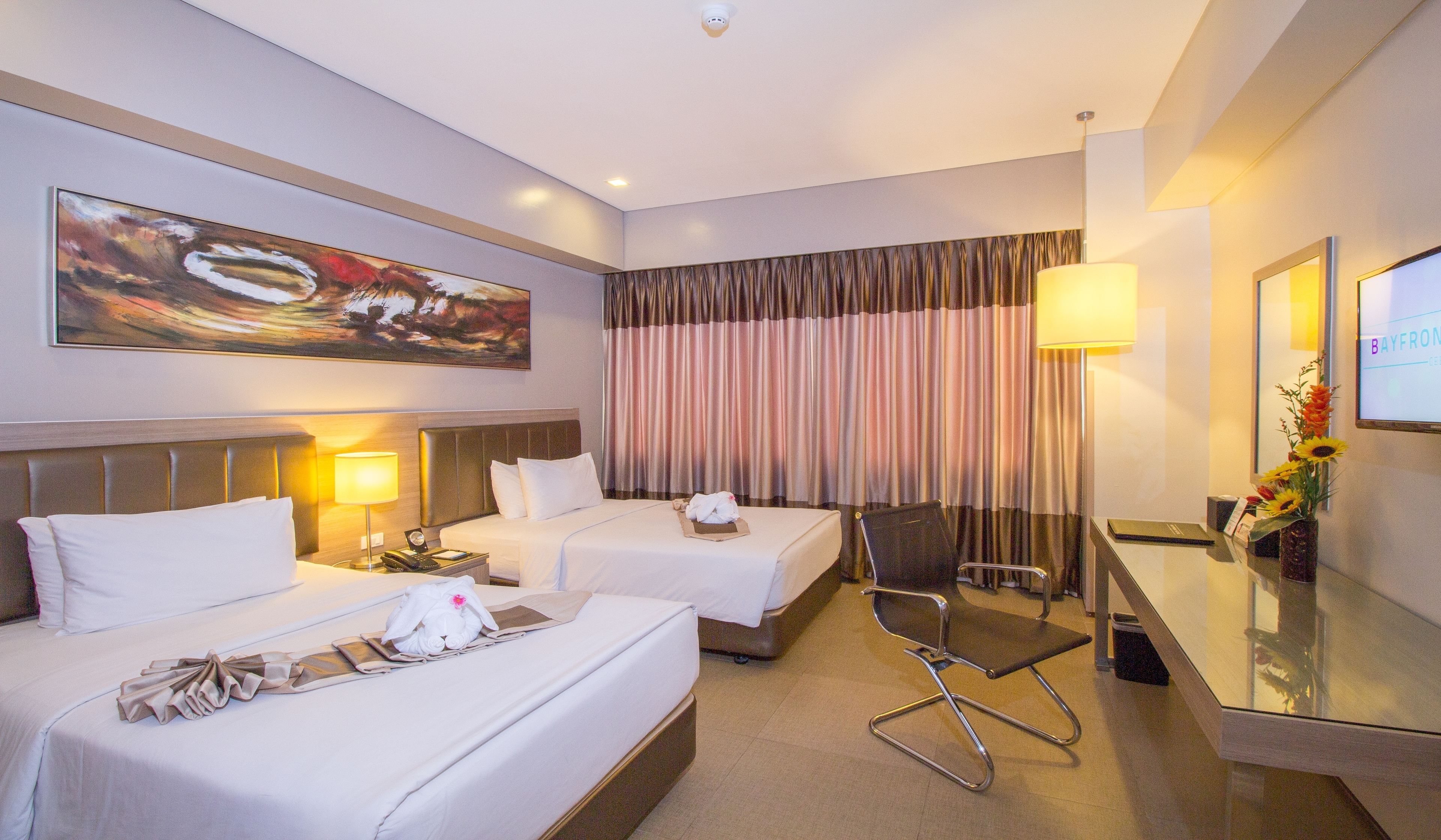 Una camera d'albergo con due letti, una scrivania, una sedia, una TV e un quadro appeso al muro.