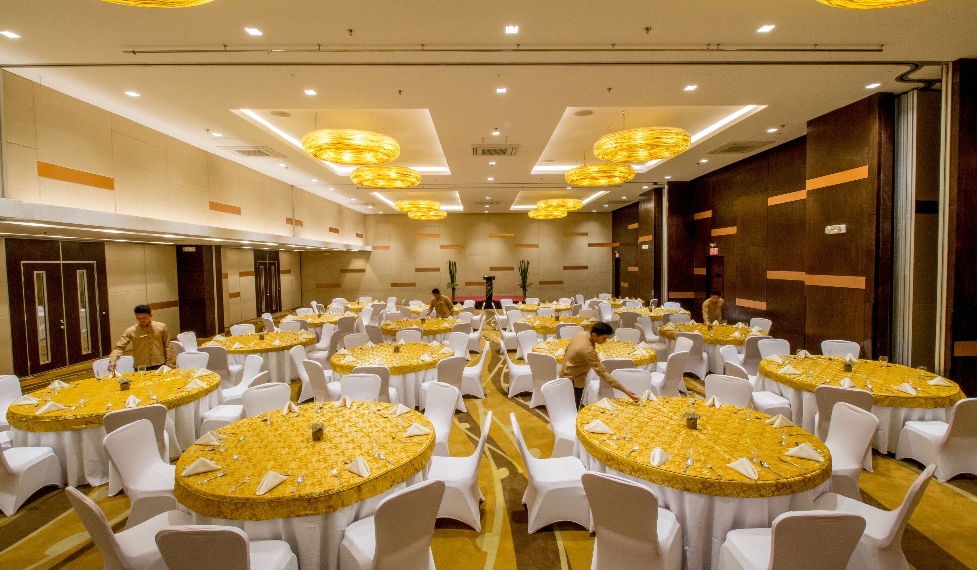 A large conference room with round tables, white chairs, and yellow tablecloths.