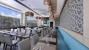 A modern restaurant with long tables, chairs, and a patterned wall.