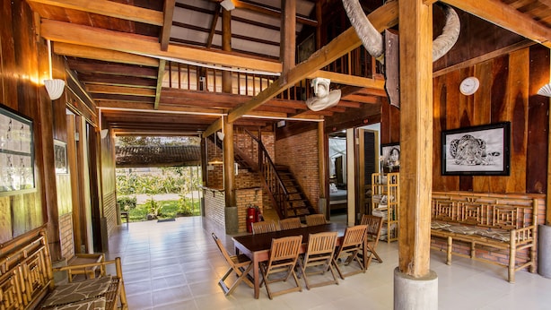 A spacious indoor area with a wooden ceiling, a dining table with chairs, a staircase, and a bench area. - Cat Tien Farm Stay (Nam Cat Tien)