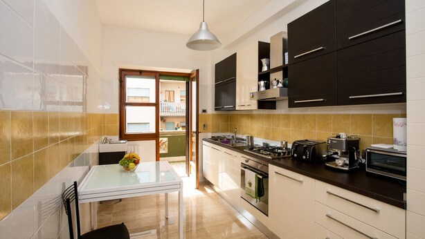 A modern kitchen with a glass table, white cabinets, and a view to the dining area. - Trastevere's Friends (Rome)