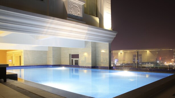 Una piscina con bordo piastrellato, circondata da un edificio con rivestimento in piastrelle e una parete vetrata che riflette il panorama urbano.