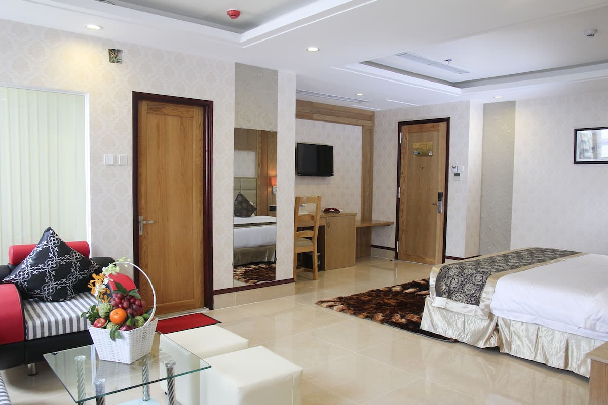 A hotel room with a bed, a sofa, a glass coffee table, a TV, and a desk.