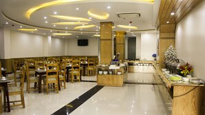 Un'ampia sala da pranzo con tavoli e sedie in legno, una postazione buffet centrale e un moderno design del soffitto con illuminazione a incasso.